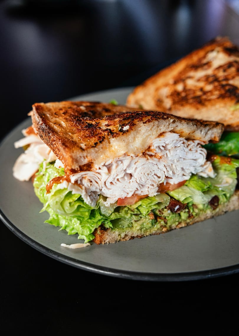 Grilled sandwich with turkey, lettuce, tomato, and guacamole on a gray plate.