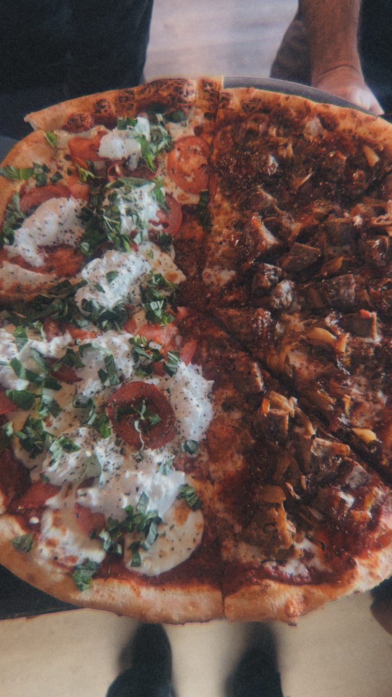 Close-up of a half-and-half pizza with fresh mozzarella, tomatoes, and basil on one side, and meat on the other.
